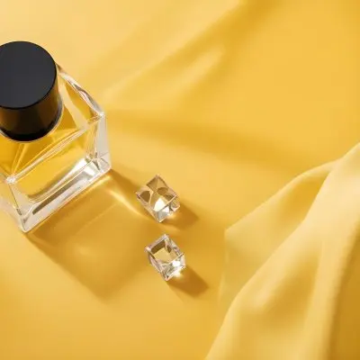 A Perfume Bottle With A Black Cap And A Small Crystal Cube On A Yellow Fabric Background 18 5ea4
