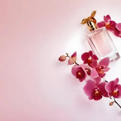 A Perfume Bottle With A Golden Cap Surrounded By Pink Orchid Flowers Placed On A Light Pink Background Product Photography 20 047e
