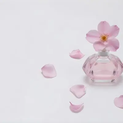 A Pink Flower Inside A Glass Perfume Bottle With Some Petals Around It On A White Background 64 107f