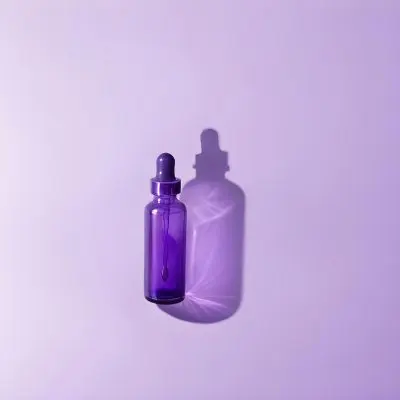 A Purple Glass Bottle With A Dropper On A Purple Background The Bottle Is Casting A Shadow To The Right 13 48bd