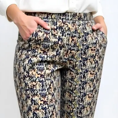 A Woman With Fair Skin Wearing Patterned Pants And A White Long Sleeved Shirt With Her Hand In Her Pocket In A Studio 7 47a2