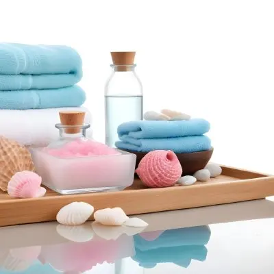 A Wooden Tray With Spa Items Including Blue Bath Salts In A Glass Bowl White And Pink Soaps A Small White Bottle And Decorative Shells There Are Also Two Rolled Towels In Light Blue And Pink The Background Is White 14 4365