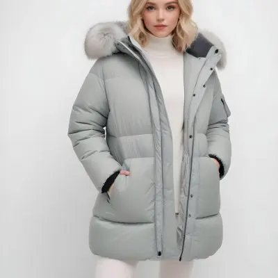 A Young Blonde Woman Wearing A Gray Puffer Jacket With A Large Fur Trimmed Hood Standing Against A White Background 18 4d74