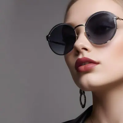 A Young Caucasian Woman With Light Skin And Long Blonde Hair Wearing Large Round Sunglasses With Dark Lenses She Has Full Lips And Is Adorned With A Dangling Earring The Background Is A Simple Gray Emphasizing Her 30 885d