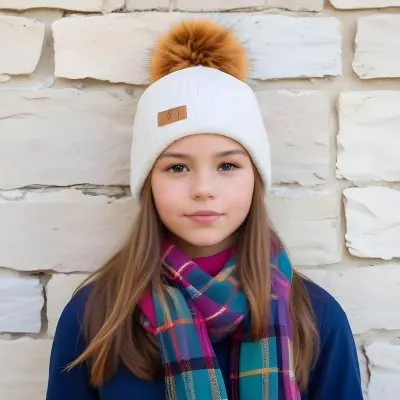 A Young Girl Approximately 12 Years Old With Light Skin And Long Brown Hair Wearing A White Beanie With A Pom Pom On Top And A Colorful Plaid Scarf The Background Consists Of A Textured Stone Wall 19 2b20
