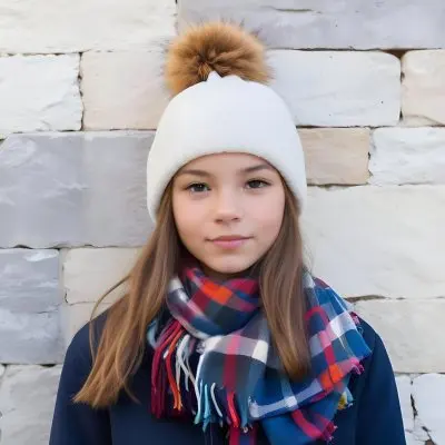 A Young Girl Approximately 12 Years Old With Light Skin And Long Brown Hair Wearing A White Beanie With A Pom Pom On Top And A Colorful Plaid Scarf The Background Consists Of A Textured Stone Wall 23 2eeb