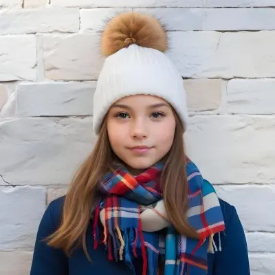 A Young Girl Approximately 12 Years Old With Light Skin And Long Brown Hair Wearing A White Beanie With A Pom Pom On Top And A Colorful Plaid Scarf The Background Consists Of A Textured Stone Wall 26 5303