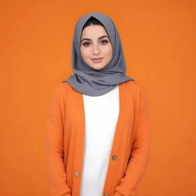 A Young Middle Eastern Woman With Dark Hair Wearing A Gray Hijab A White Sweater And A Orange Cardigan Standing Against A Orange Background 3 D4f8