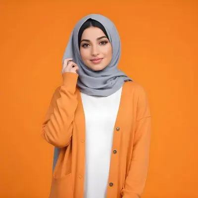 A Young Middle Eastern Woman With Dark Hair Wearing A Gray Hijab A White Sweater And A Orange Cardigan Standing Against A Orange Background 4 A5e5