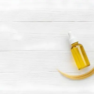 Bottle Of Yellow Hair Oil With A White Cap And A Strand Of Blonde Hair On A White Wooden Table 41 3ca7