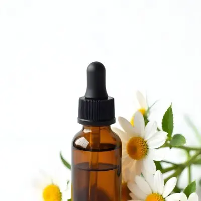 Brown Glass Bottle With Dropper Surrounded By Chamomile Flowers White Background 3 11e4