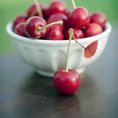 A Bowl Full Of Red Cherries With A Red Leaf On A Wooden Table With A Blurred Red Background 5 3db6