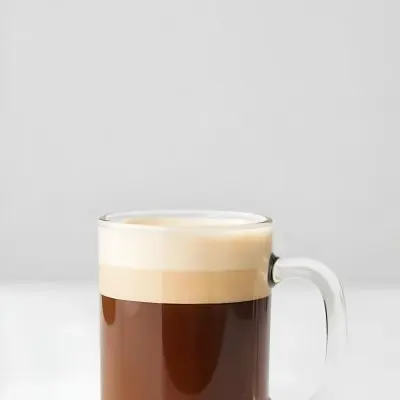 A Glass Of Dark Coffee With A Layer Of Light Brown Foam On Top Against A Plain White Background 1 25d7