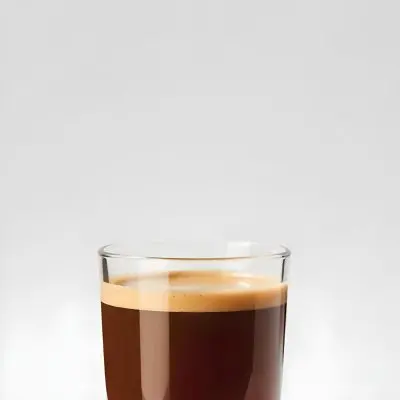 A Glass Of Dark Coffee With A Layer Of Light Brown Foam On Top Against A Plain White Background 14 C646