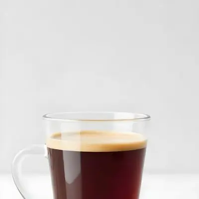 A Glass Of Dark Coffee With A Layer Of Light Brown Foam On Top Against A Plain White Background 16 6eea