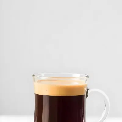 A Glass Of Dark Coffee With A Layer Of Light Brown Foam On Top Against A Plain White Background 17 66b4