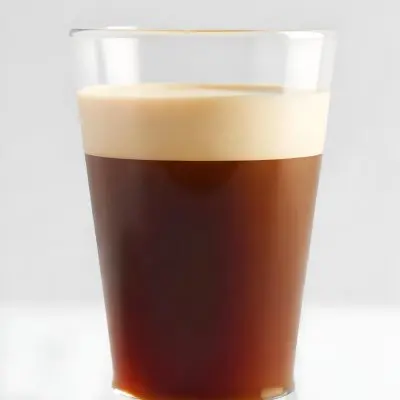 A Glass Of Dark Coffee With A Layer Of Light Brown Foam On Top Against A Plain White Background 5 75ab