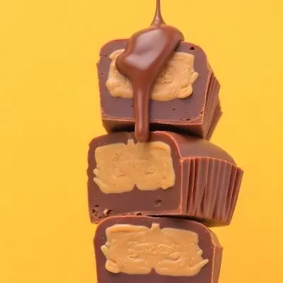 Stack Of Three Chocolate Peanut Butter Cups With Chocolate Syrup Being Poured On Top In A Yellow Background 19 6e5a