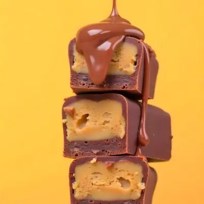 Stack Of Three Chocolate Peanut Butter Cups With Chocolate Syrup Being Poured On Top In A Yellow Background 22 0c25