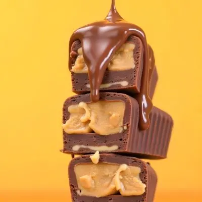 Stack Of Three Chocolate Peanut Butter Cups With Chocolate Syrup Being Poured On Top In A Yellow Background 27 D296