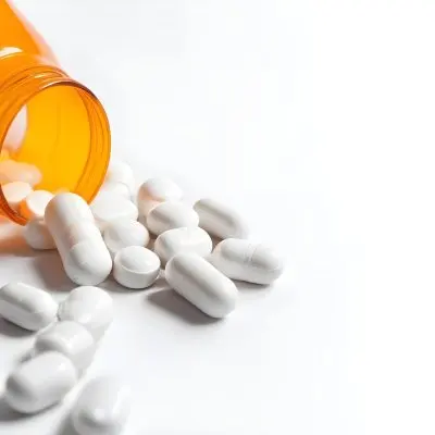 White Pills Spilling Out Of An Orange Pill Bottle On A White Surface Studio Shot 1 306b