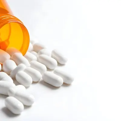 White Pills Spilling Out Of An Orange Pill Bottle On A White Surface Studio Shot 4 6cde