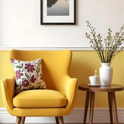Yellow Armchair With A Flower Pillow Next To A Wooden Table With A Vase Of White Flowers A Cup Of Tea And A Candle With A Yellow Wall And A Framed Picture In The Background 21 D326