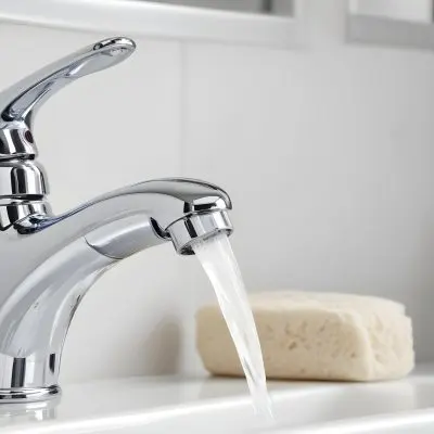 A Chrome Faucet With Water Running In A White Sink With A Soap Dish In The Background 20 E1e7