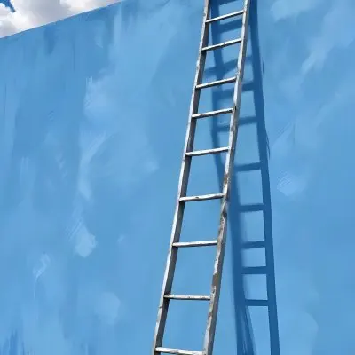 A Silver Ladder Leaning Against A Blue Wall Under A Blue Sky With Some Clouds The Ladder Is Casting A Shadow On The Wall 5 Aa32
