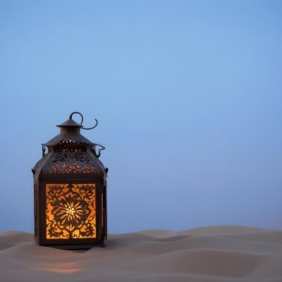 An Ornate Metal Lantern With Intricate Floral Cutouts Casting A Warm Glow On A Sandy Surface Against A Soft Gradient Blue Background 2 D0e7