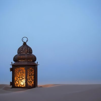 An Ornate Metal Lantern With Intricate Floral Cutouts Casting A Warm Glow On A Sandy Surface Against A Soft Gradient Blue Background 20 3a6c