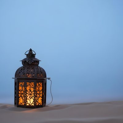 An Ornate Metal Lantern With Intricate Floral Cutouts Casting A Warm Glow On A Sandy Surface Against A Soft Gradient Blue Background 29 2d81