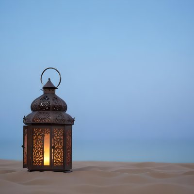 An Ornate Metal Lantern With Intricate Floral Cutouts Casting A Warm Glow On A Sandy Surface Against A Soft Gradient Blue Background 7 2288