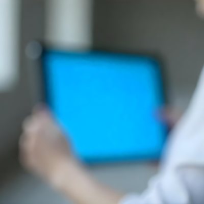 A Person Holding A Tablet With A Blank Blue Screen The Background Is Blurred And Out Of Focus The Person Is Wearing A White Shirt 2 4c89